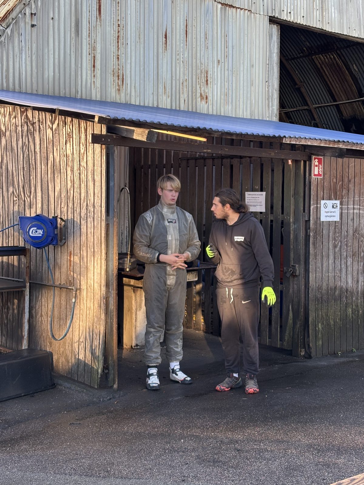 Knud-Magnus i køredragt taler med mekanikeren foran depotet